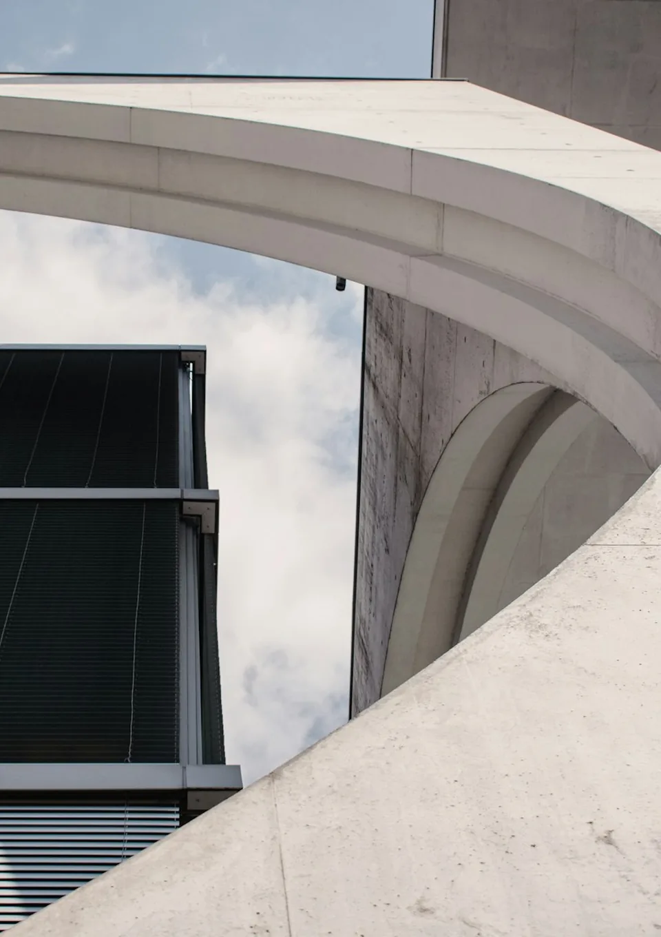 Curved concrete canopy meeting a glass facade against a pale sky