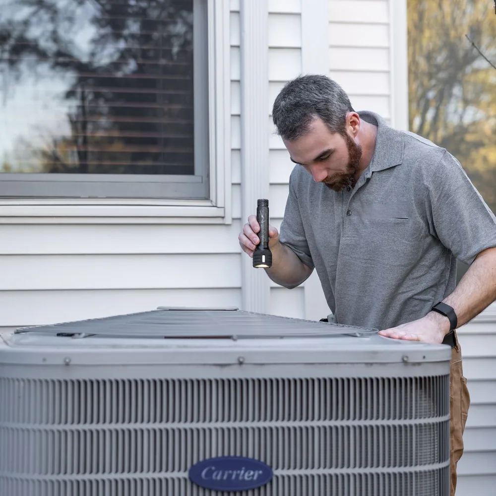 Service engineer inspecting an outdoor condensing unit with a torch