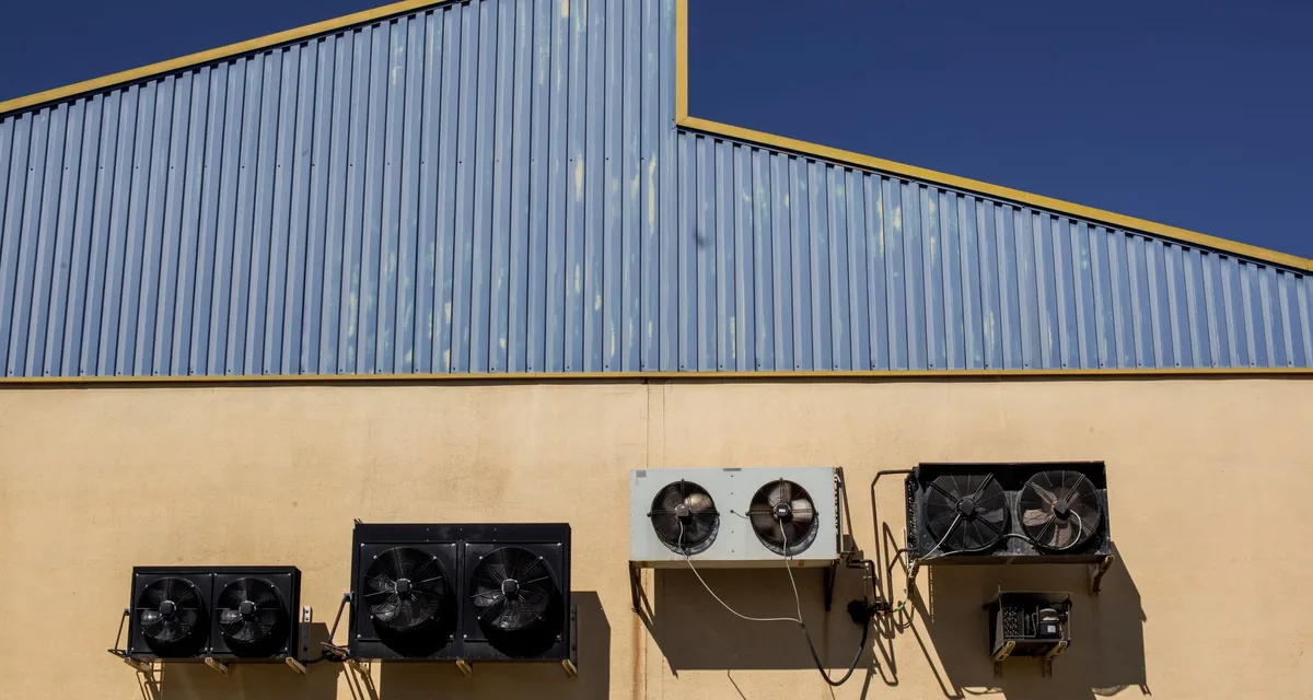 Condensing units mounted in a clean row on a commercial building wall under a blue sky